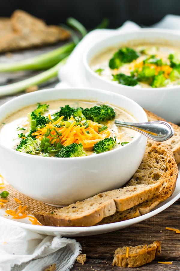 Broccoli cheddar soup in a bowl with garlic bread surrounding it.