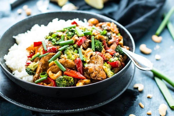 A black bowl filled with gluten-free chicken with cashew nuts and rice.