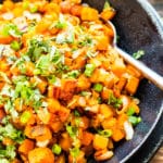 Pan fried sweet potatoes in a bowl with chopped green onions as a garnish.