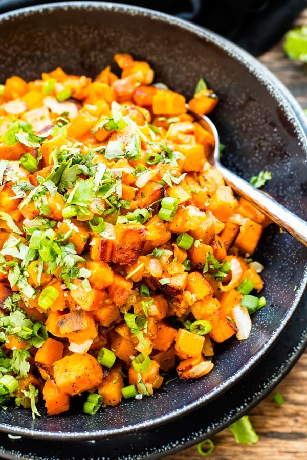 Pan fried sweet potatoes in a bowl with chopped green onions as a garnish.