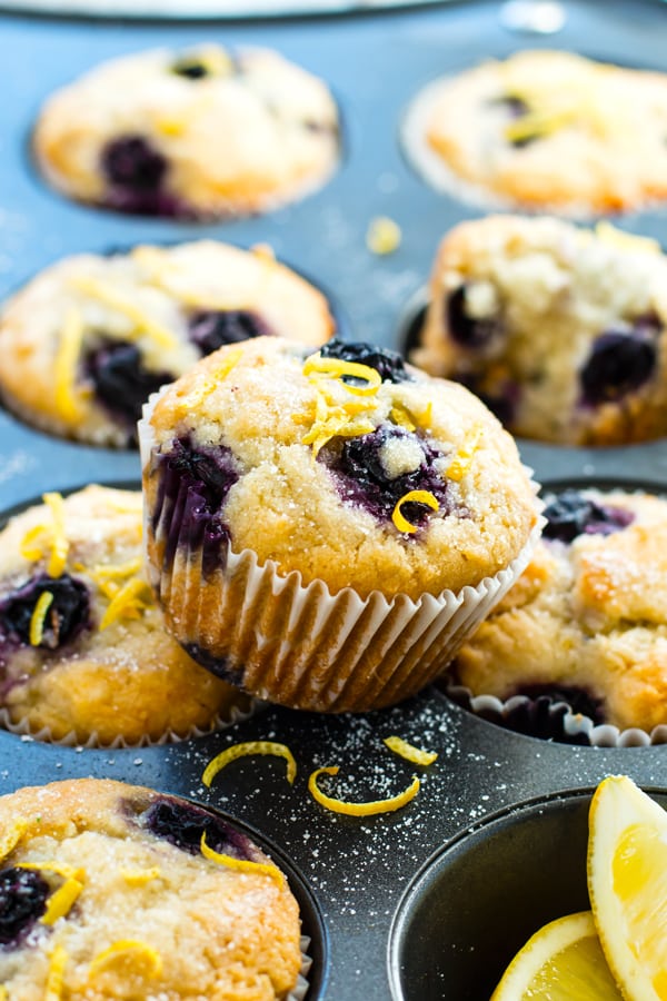 A healthy blueberry muffin recipe sitting on top of a muffin pan with lemons.