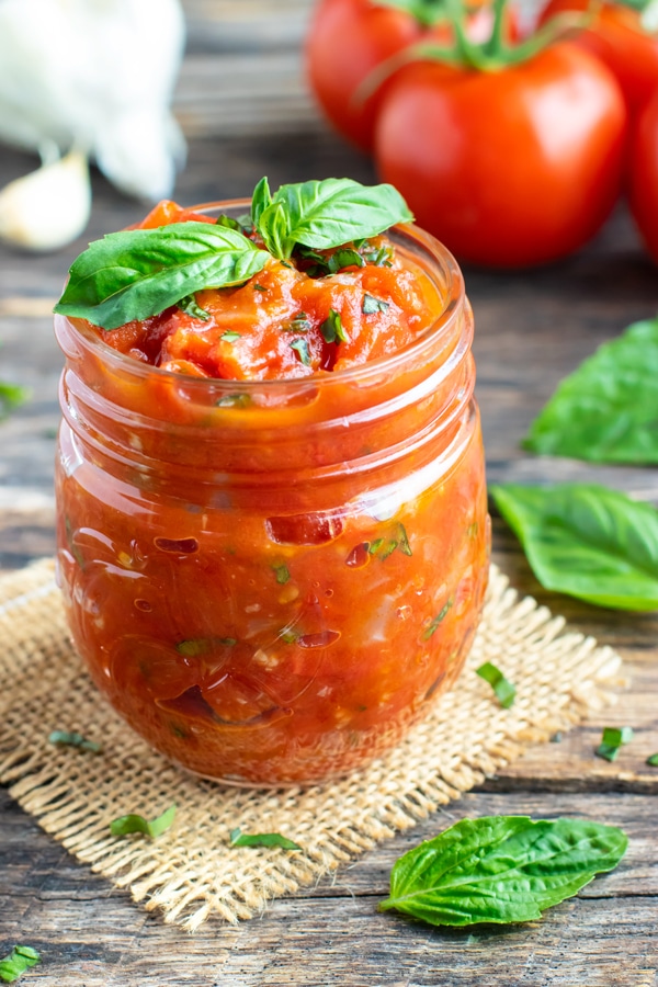 Homemade spaghetti sauce in a clear jar with basil and tomatoes around it.