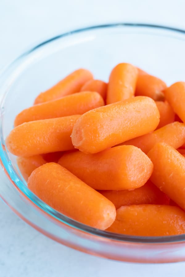 A glass bowl full of mini baby carrots.