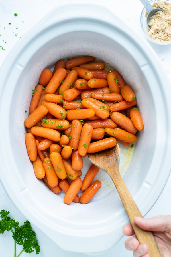 A 6-quart Crock-Pot with baby carrots that have been cooked in a honey, brown sugar, and butter sauce until perfectly glazed.