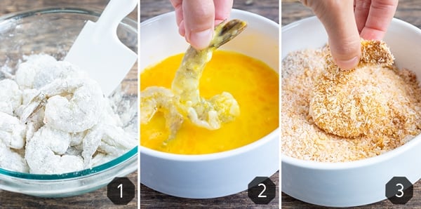 A bowl of shrimp coated in flour, shrimp in an egg wash, and then being dipped in a coconut and bread crumb mixture.