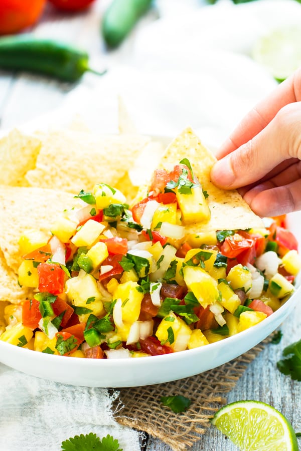 A hand using a tortilla chip to scoop a serving of a Pineapple Pico de Gallo recipe for lunch.