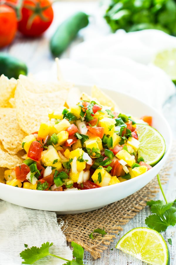 Fresh vegetables in the background of bowl filled with Pineapple Pico de Gallo.