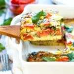 A wooden serving spoon holding a serving of a Baked Frittata with Pesto, Tomatoes, and Goat Cheese.