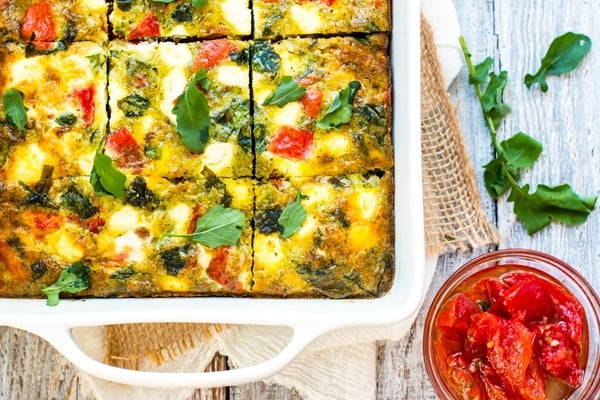 A gluten-free egg frittata with pesto, tomatoes, and goat cheese in a casserole dish for breakfast.