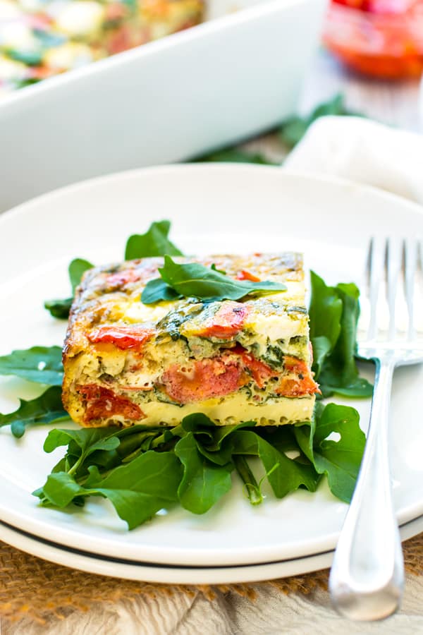 A serving of a baked frittata recipe with pesto, tomatoes, and goat cheese on a white plate.