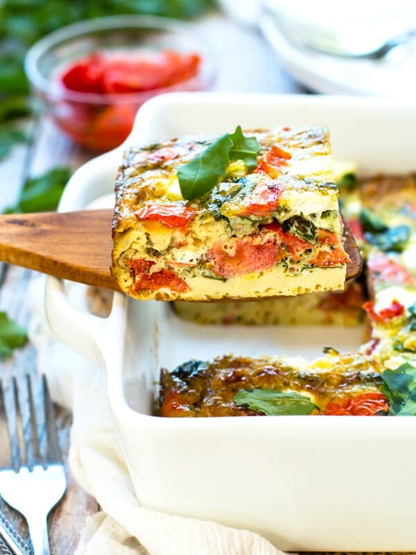 A wooden serving spoon holding a serving of a Baked Frittata with Pesto, Tomatoes, and Goat Cheese.
