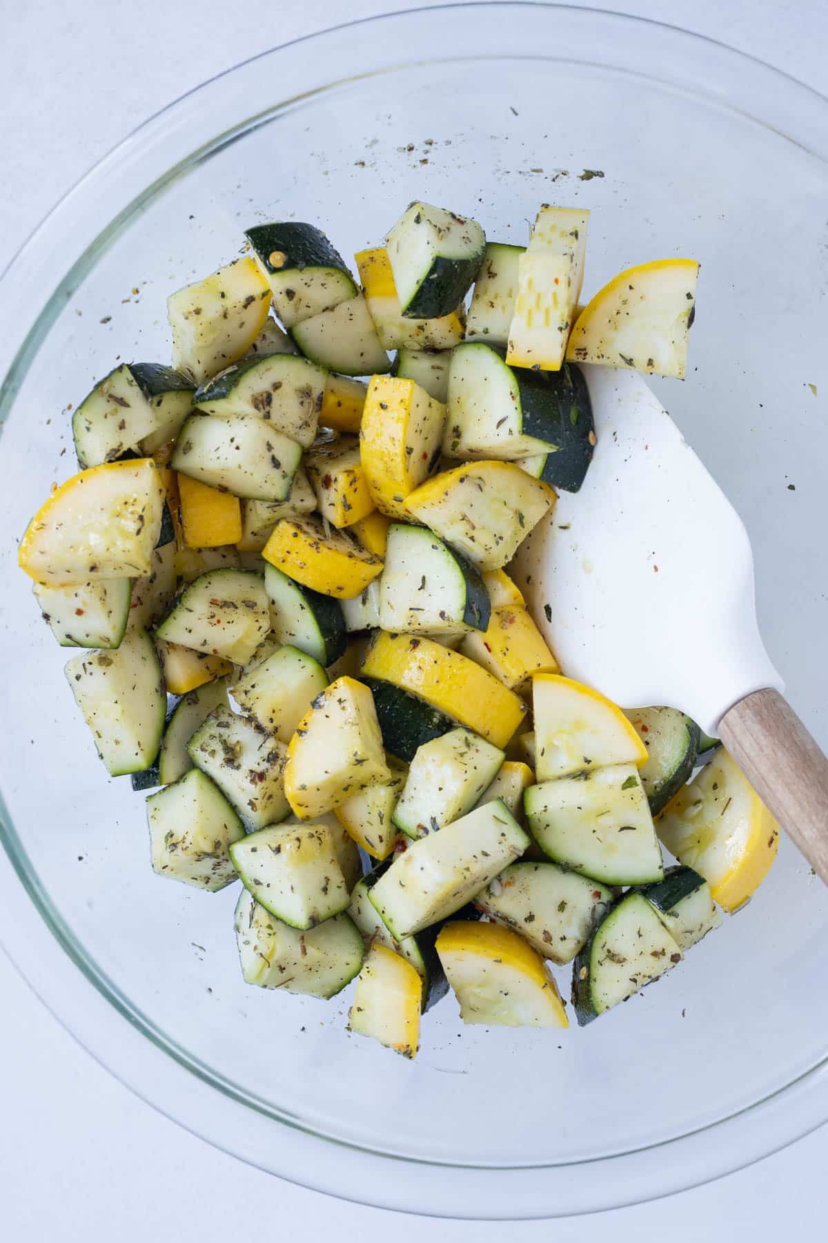 Yellow squash and zucchini are seasoned in a bowl before roasting.
