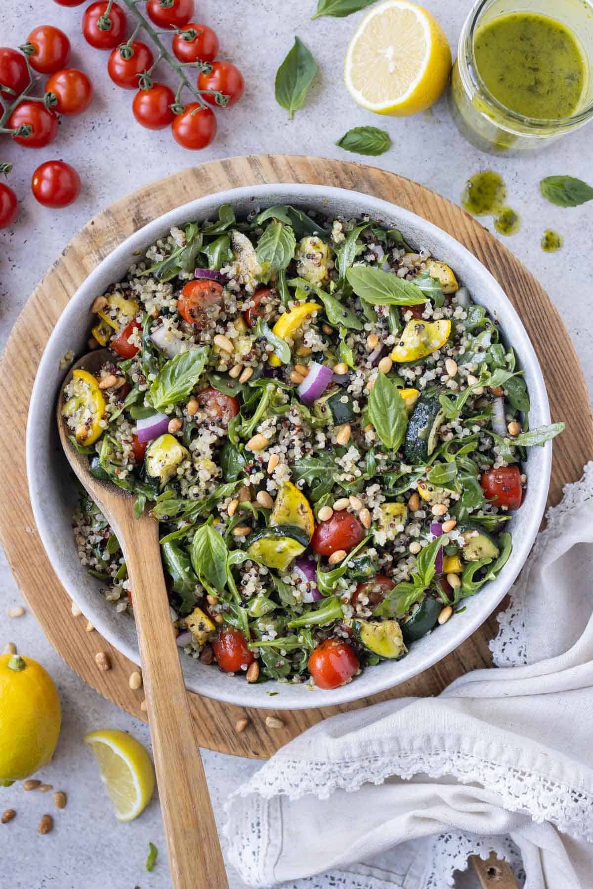 A wooden spoon scoops up a serving of a summer quinoa salad with lemon vinaigrette from a serving bowl.
