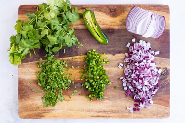 Finely chopped cilantro, jalapeno, and red onion on a wooden cutting board.