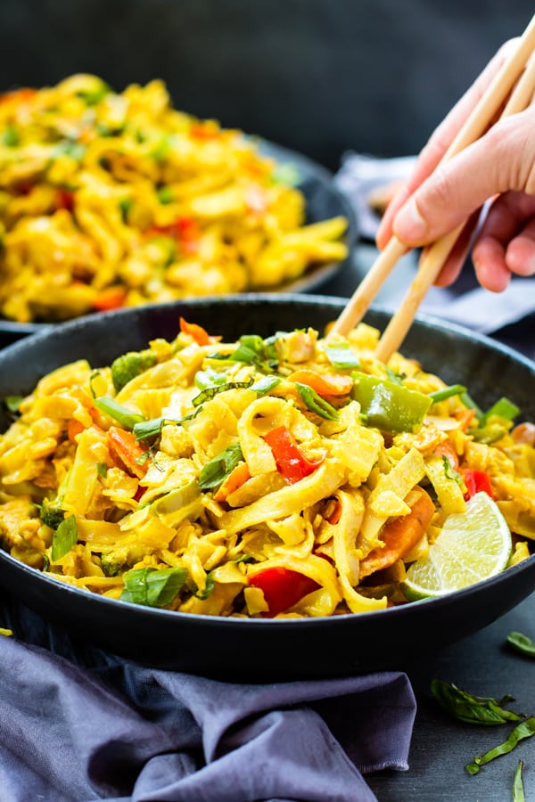 A hand guiding using chopsticks in a bowl filled with Thai Curry Noodles for dinner.