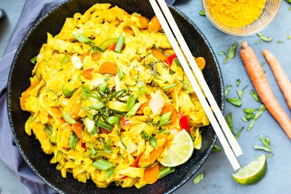 Gluten-free curry noodles recipe in a black bowl with chopsticks.