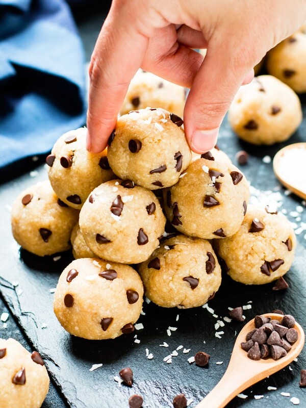 A pair of fingers picking up a ball of chocolate chip energy bites with a wooden spoon.
