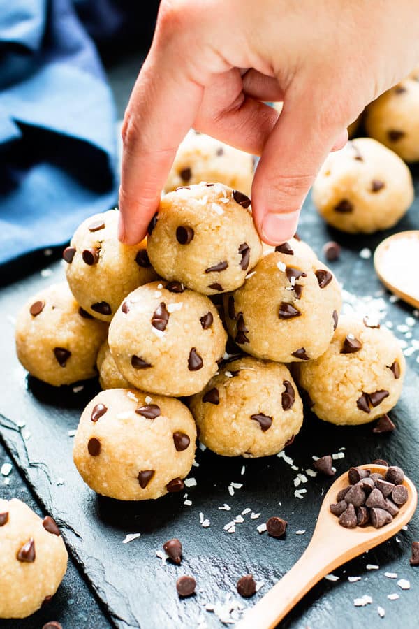 A pair of fingers picking up a ball of chocolate chip energy bites with a wooden spoon.
