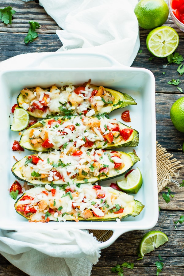 An overhead picture of zucchini boats with chicken and lime on a table ready for dinner.