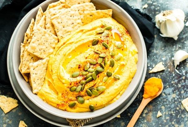 Gluten-free Savory Pumpkin Hummus in a bowl with crackers and seeds.