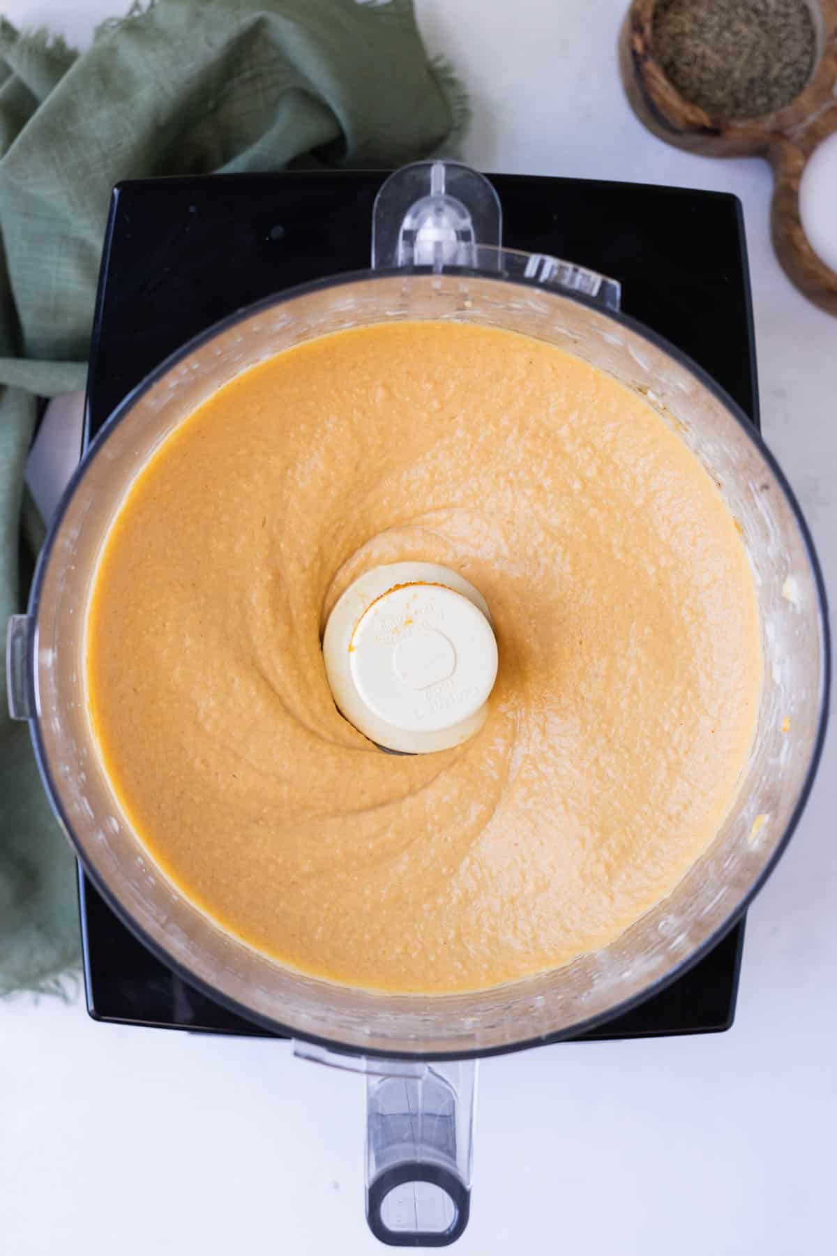 Pumpkin hummus is pureed in a food processor until smooth and creamy.