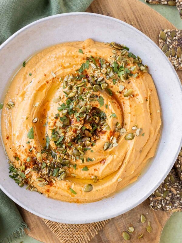 A savory pumpkin hummus recipe is in a white bowl with roasted pumpkin seeds on top.