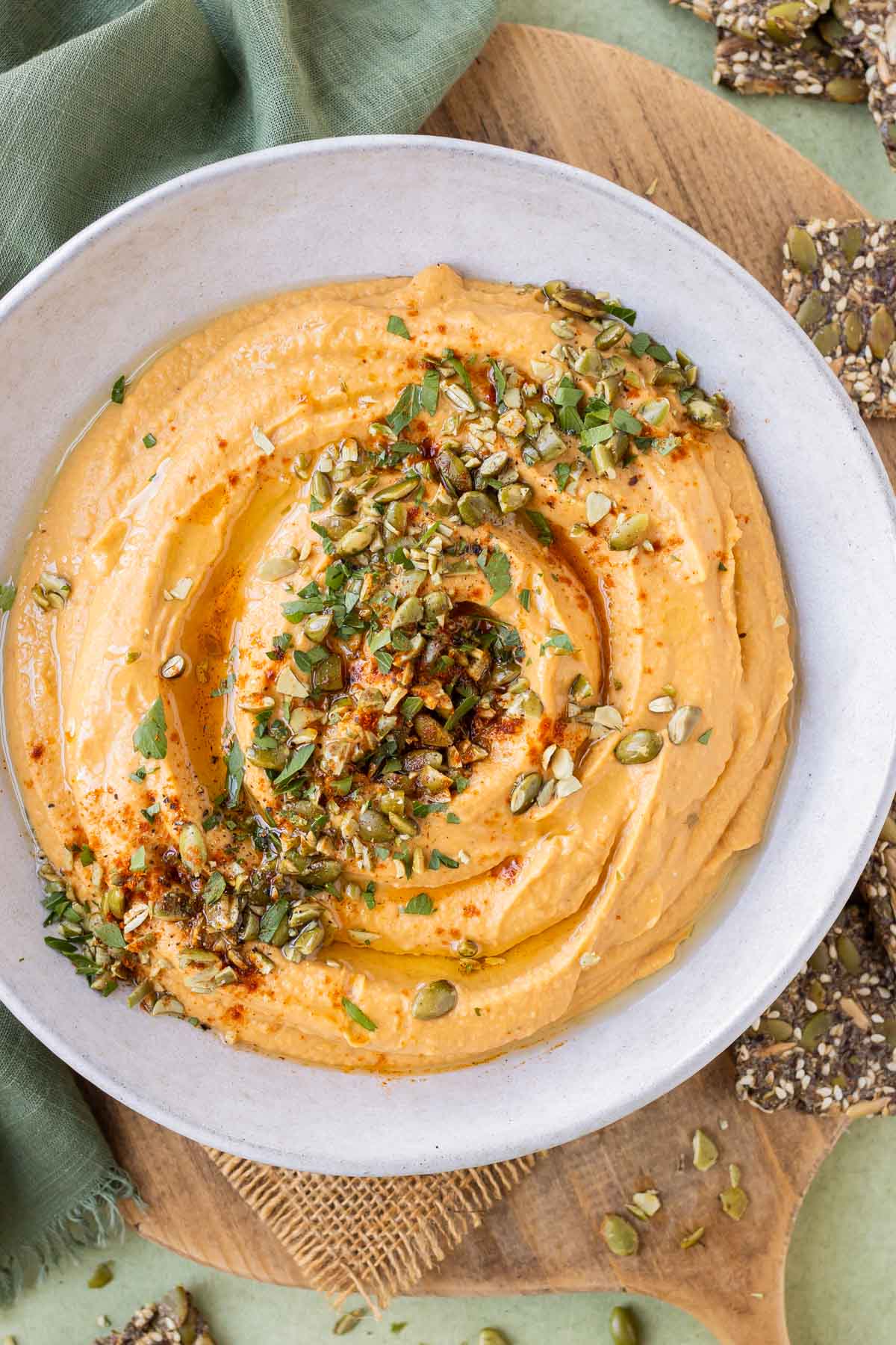 A savory pumpkin hummus recipe is in a white bowl with roasted pumpkin seeds on top.