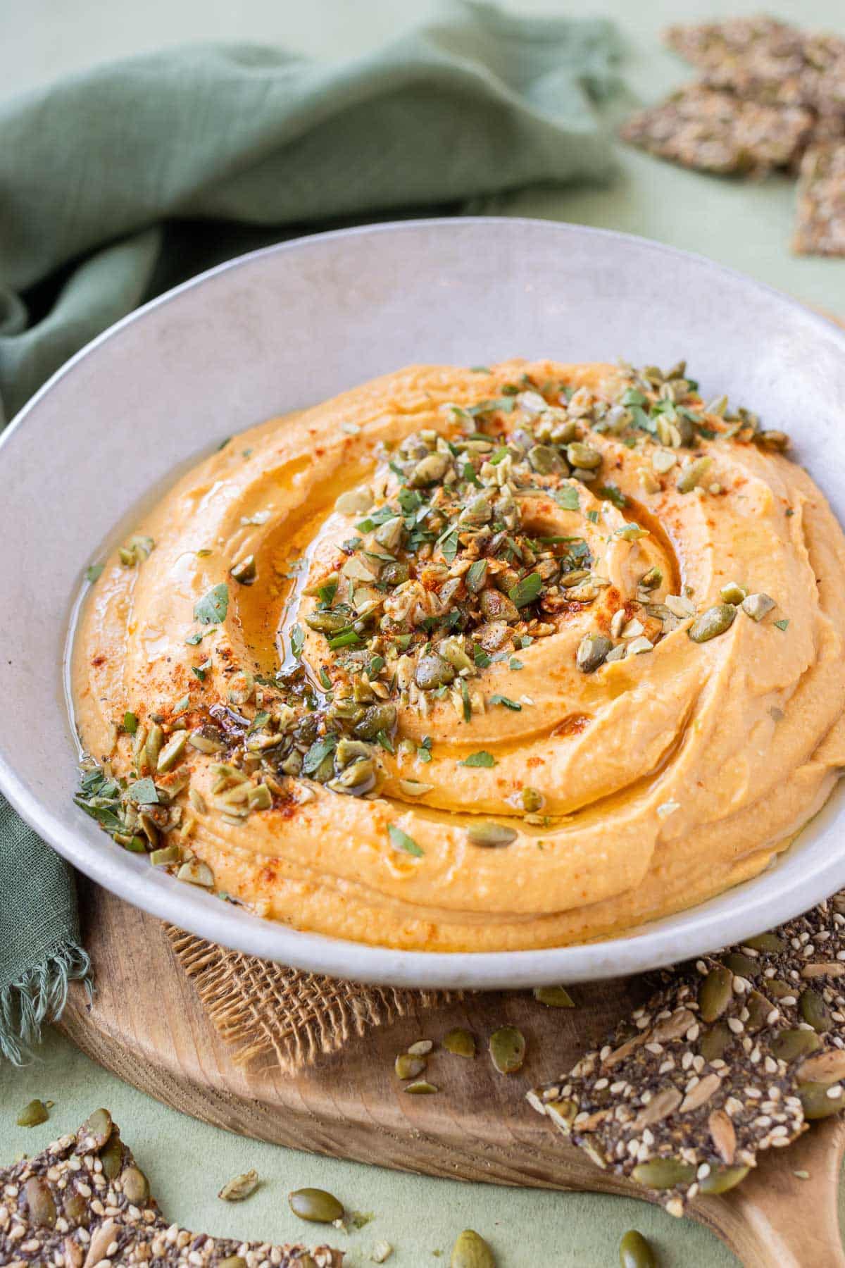 A white bowl is full of homemade pumpkin hummus with seeds and herbs on top.