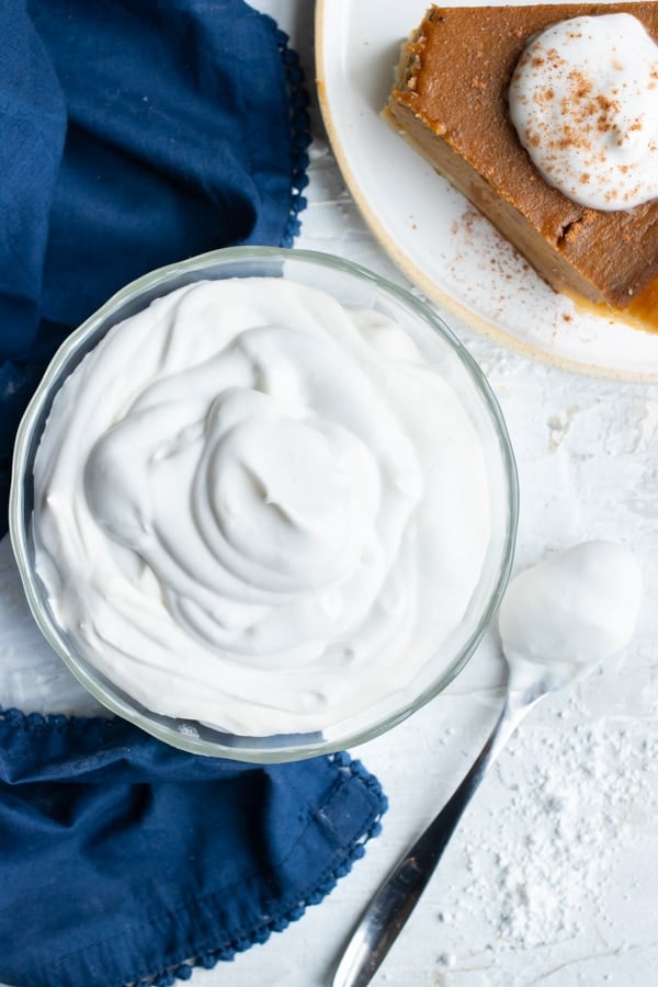 A small bowl full of whipped coconut cream next to a piece of pumpkin pie.