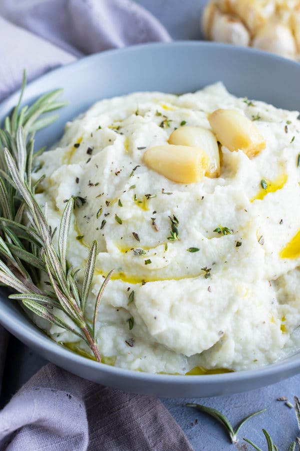 A grey bowl full of mashed cauliflower with roasted garlic and herbs.