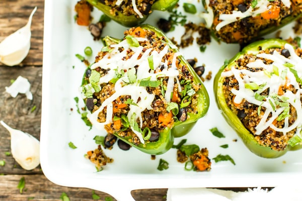 Vegan stuffed peppers recipe with black bean and quinoa on a white serving tray.