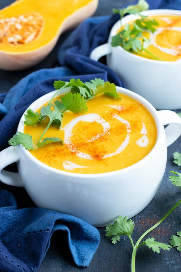 A serving bowl full of healthy, Paleo, Whole and vegan roasted butternut squash soup with a drizzle of coconut milk and a cilantro sprig on top.
