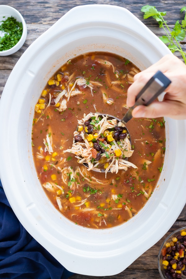 A ladle scooping out healthy tortilla soup from a Crock-Pot.
