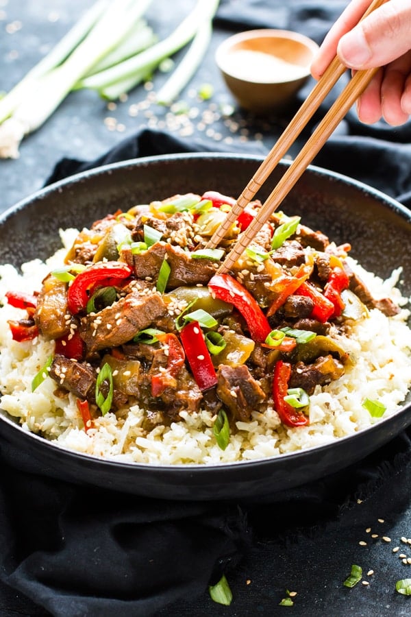 Gluten-free Slow Cooker Beef Teriyaki in a black bowl with chopsticks in one hand.