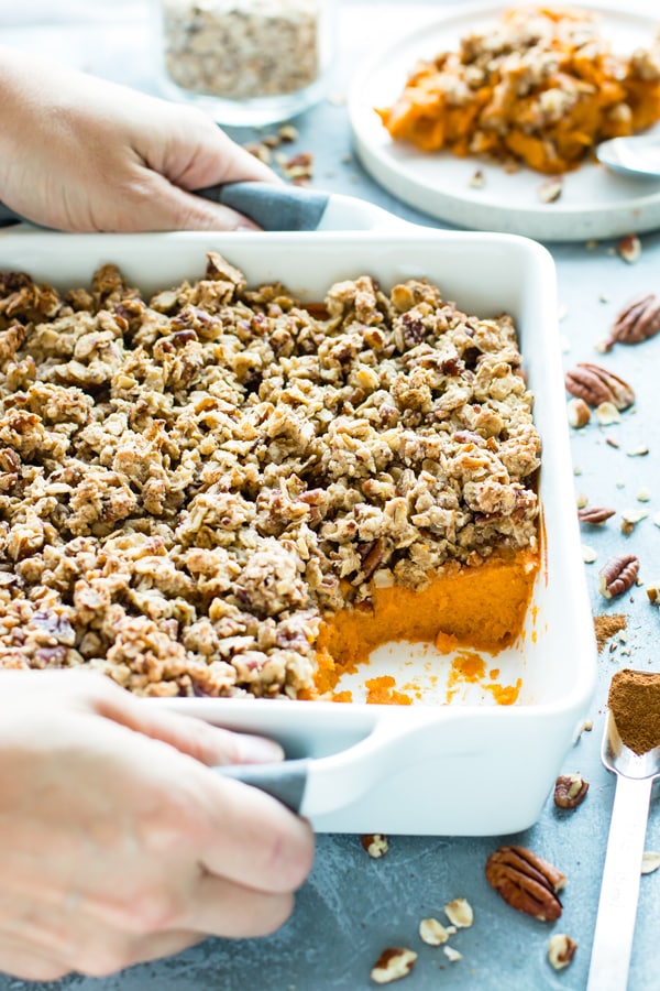 Two hands carrying a dish full of Healthy Sweet Potato Casserole with Pecans and Oats.
