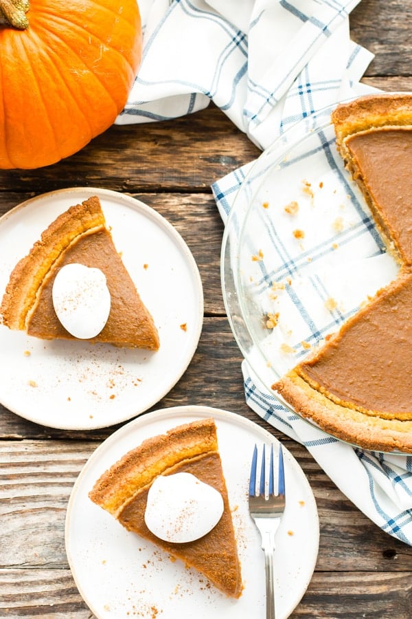 Two pieces of paleo pumpkin pie on white plates with a pumpkin on the side.