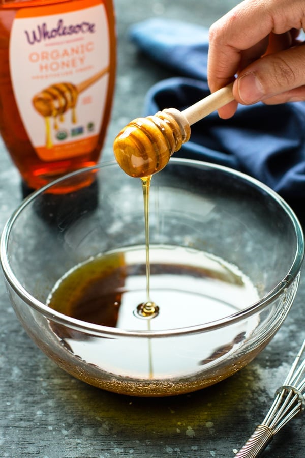 A bottle of Wholesome Organic Honey next to a bowl filled with honey.
