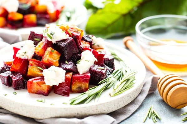 Roasted beets with honey ricotta on a speckled plate next to a honey dipper.