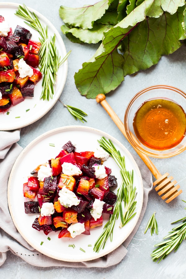 Two white plates full of baked beets with honey ricotta and herbs for a healthy side dish.