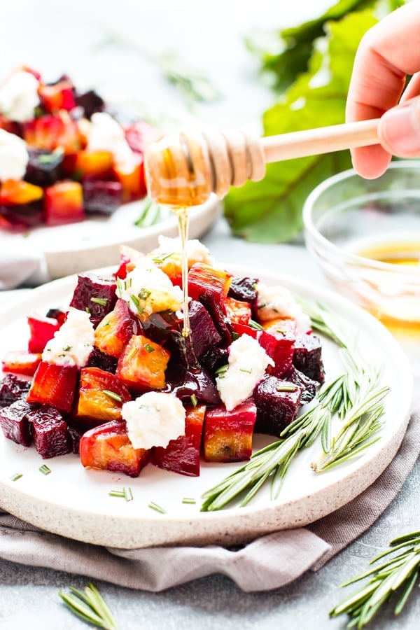 Oven-Roasted Beets with Honey Ricotta & Herbs RECIPE served on a white dish with a drizzle of honey.