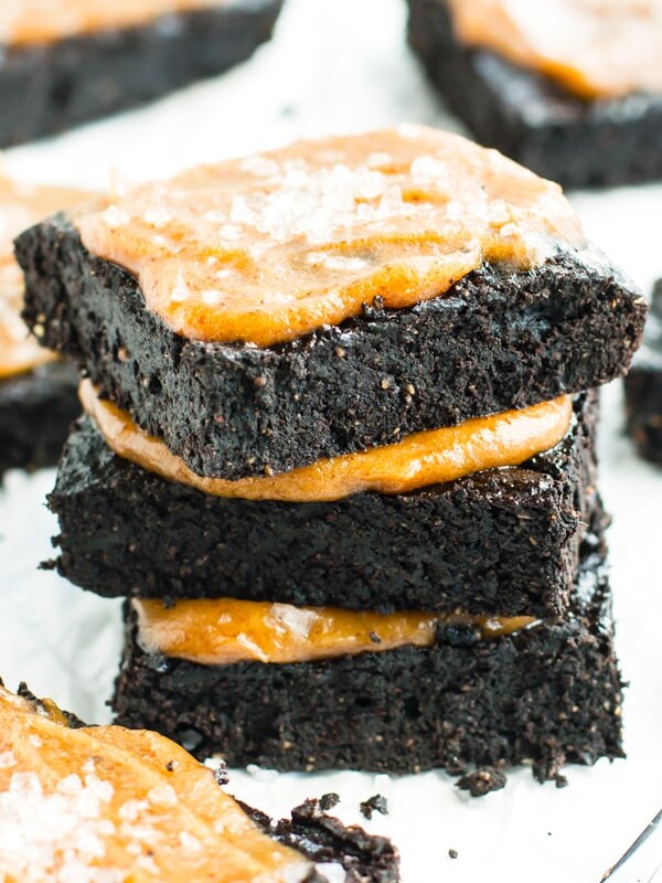 A stack of gluten-free Salted Caramel Fudgy Paleo Brownies on a white table with a caramel topping.