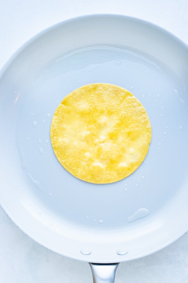 Corn tortillas are cooked on a skillet before being filled.