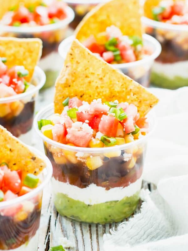 A collection of plastic cups containing healthy 7-layer dips with tortilla chips as a topping.
