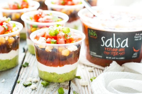 Individual cups filled with a seven layer dip recipe using Fresh Cravings salsa.