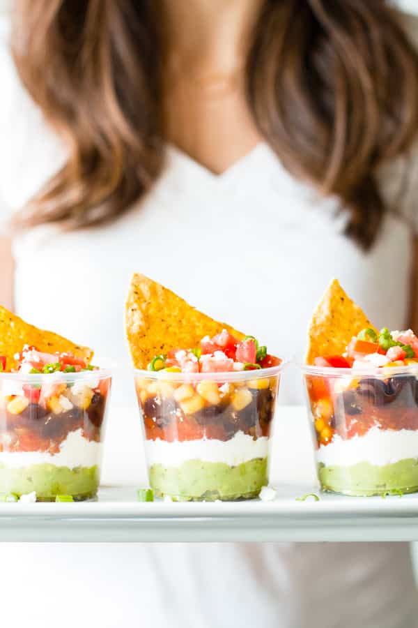 A woman holding a tray of gluten-free 7 layer dip cups for a healthy lunch.