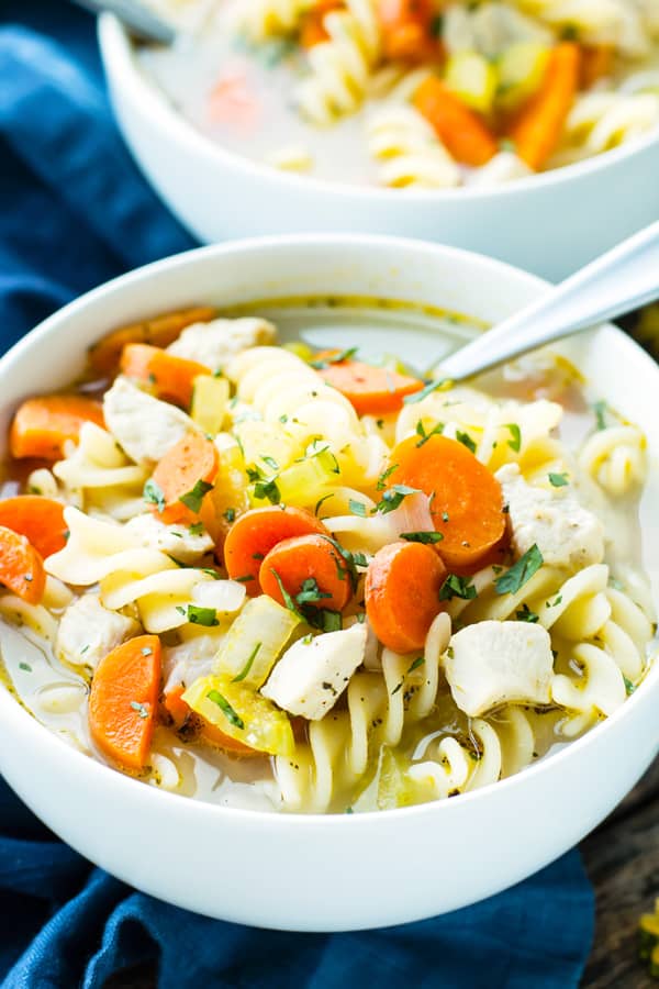 A bowl filled with gluten-free chicken soup with a spoon inside.