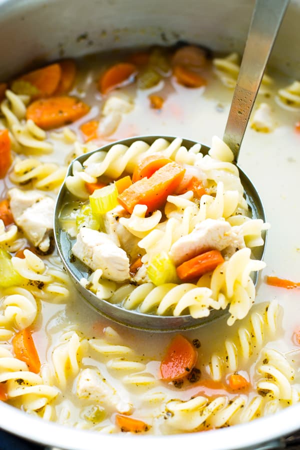 A ladle filled with healthy chicken noodle soup from a pot for a delicious dinner.