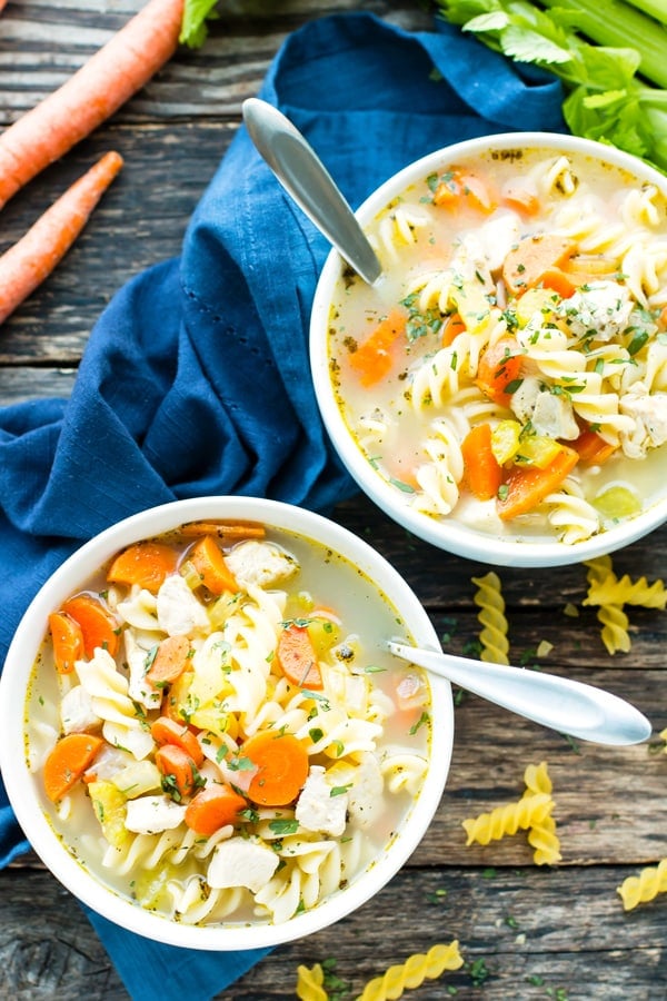 Two bowls filled with a gluten-free chicken noodle soup recipe sitting next to a blue napkin.