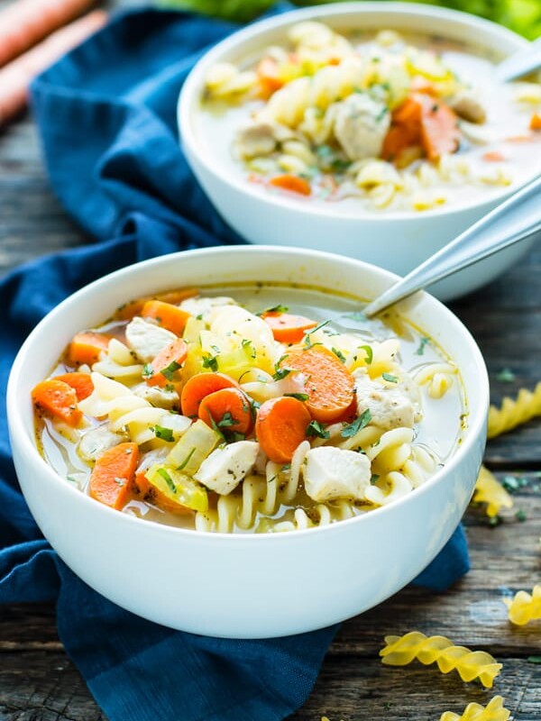 Two white bowls filled with 30-Minute Easy Chicken Noodle Soup with a blue napkin on the side.