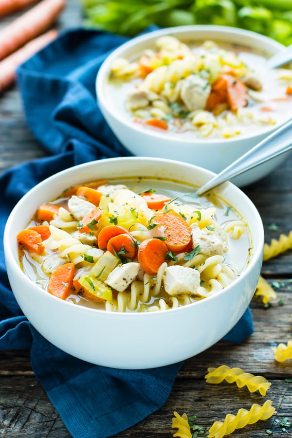 Two white bowls filled with 30-Minute Easy Chicken Noodle Soup that is a healthy soup recipe with a blue napkin on the side.